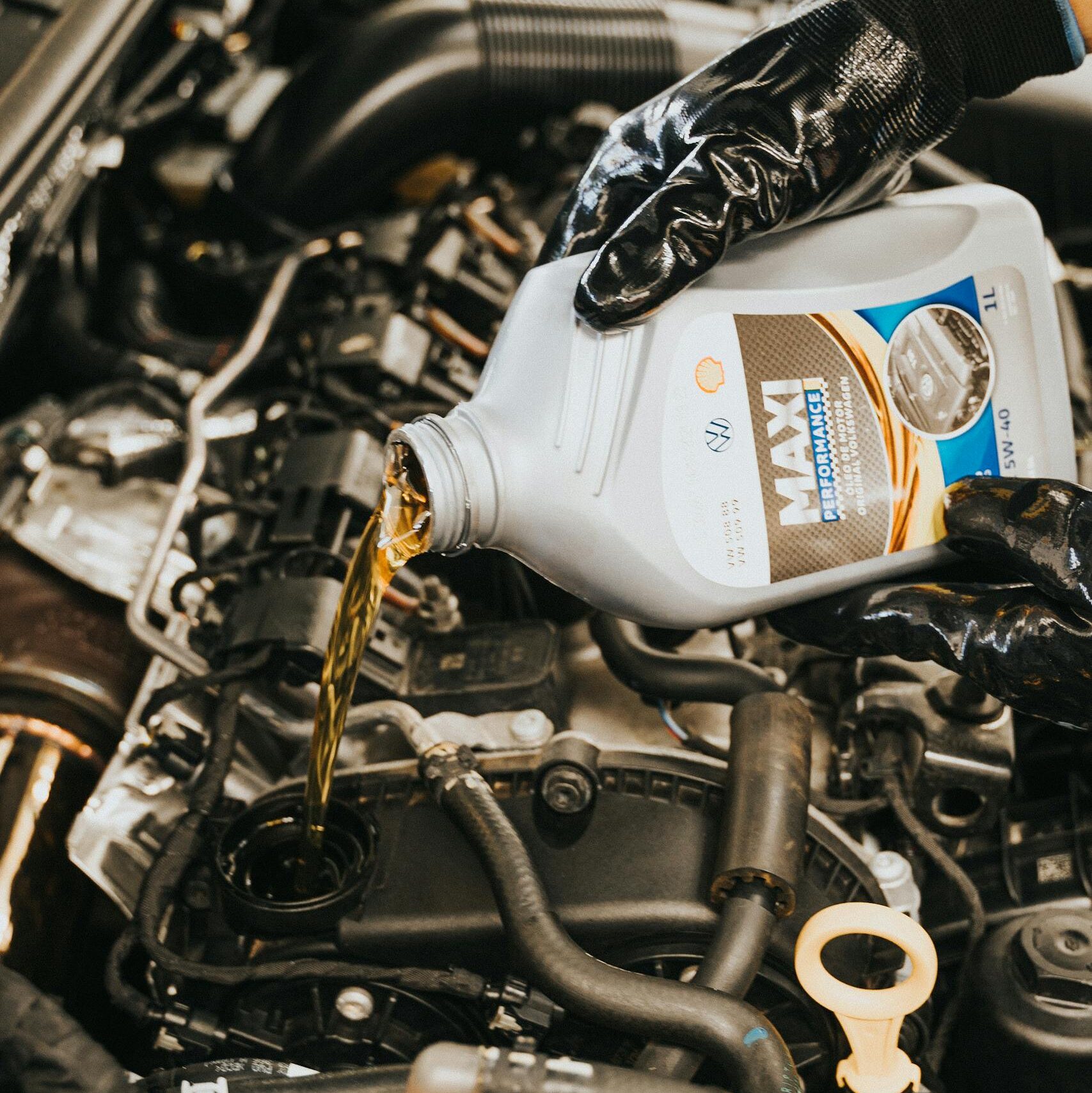 Close-up of mechanic pouring engine oil into car engine with gloved hands, showcasing automotive maintenance.